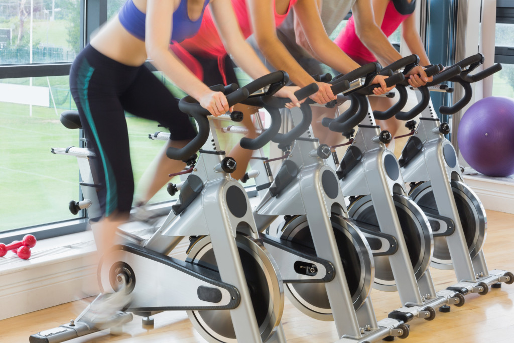 Four people working out using stationary bikes in a gym.